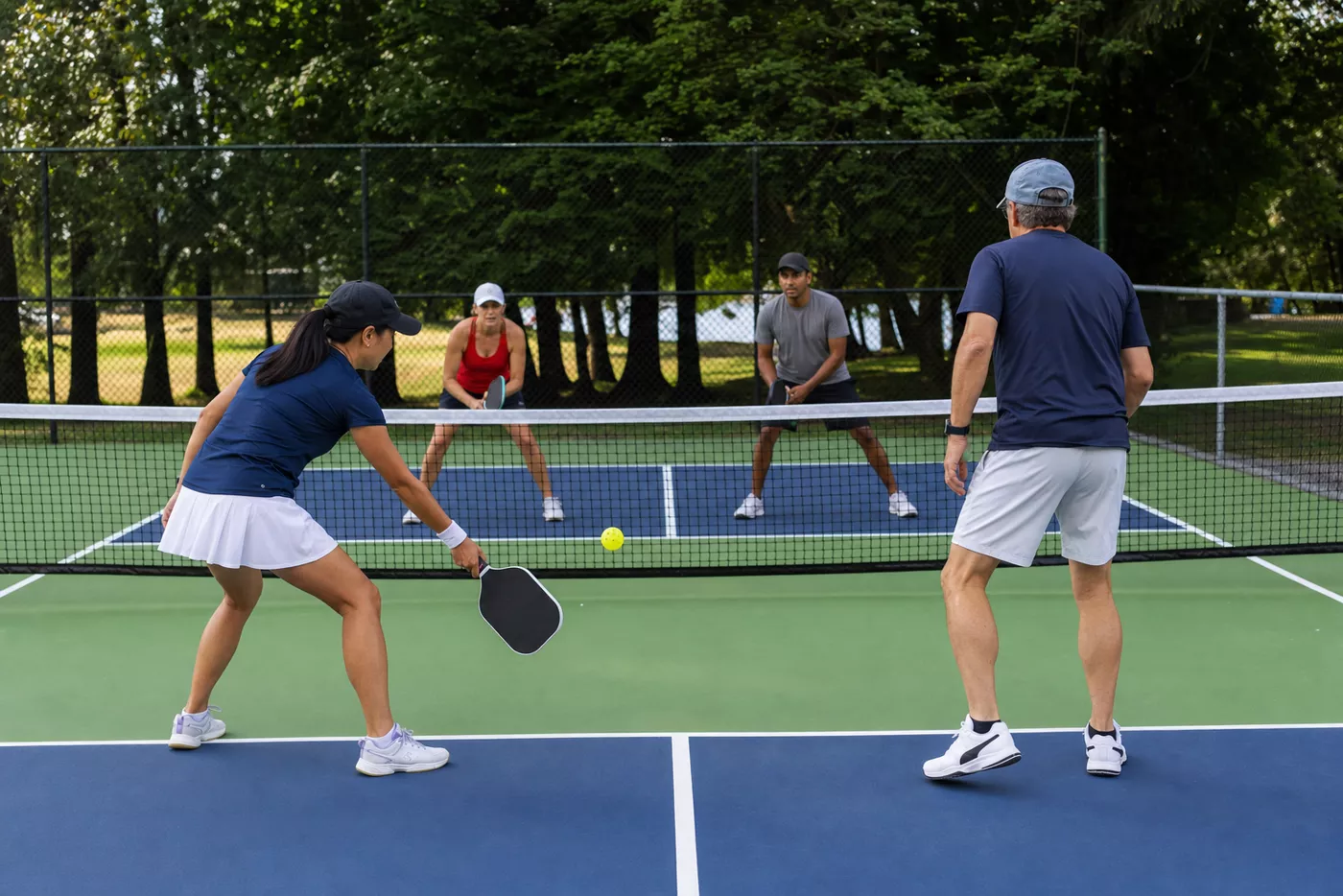Four pickleball players dinking from behind the non-volley-zone kitchen line
